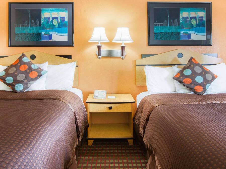 Habitación de hotel con dos camas, cada una con una almohada, una mesita de noche con un teléfono y dos lámparas fijadas a la pared.