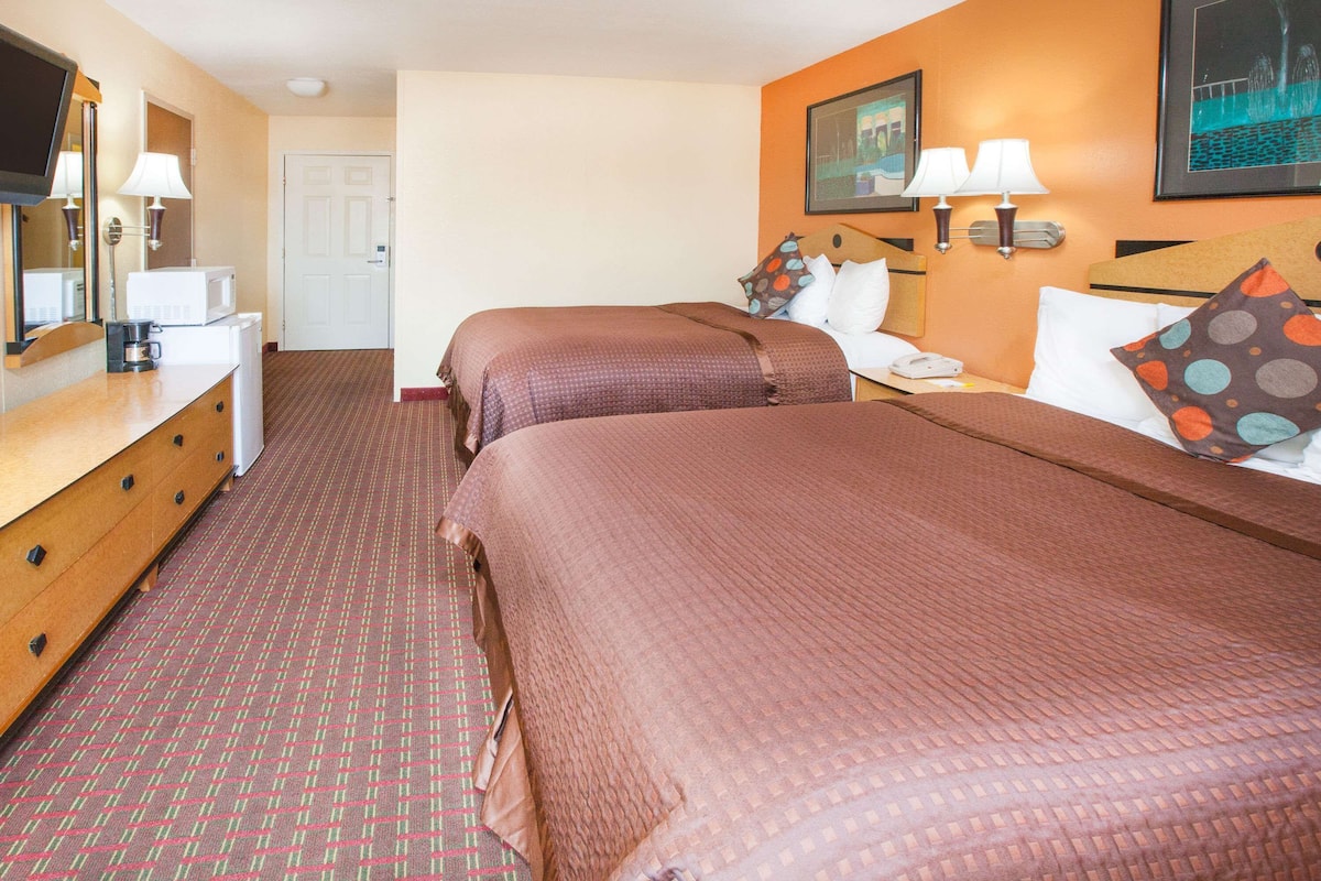 A hotel room with two beds, a wooden dresser, a microwave, and a television.