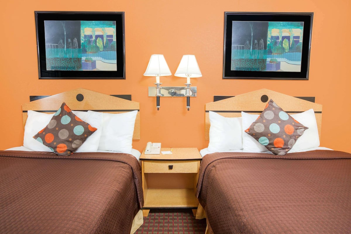 A hotel room with two beds, each with a pillow and a nightstand with a lamp.