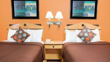 A hotel room with two beds, each with a pillow and a nightstand with a lamp.