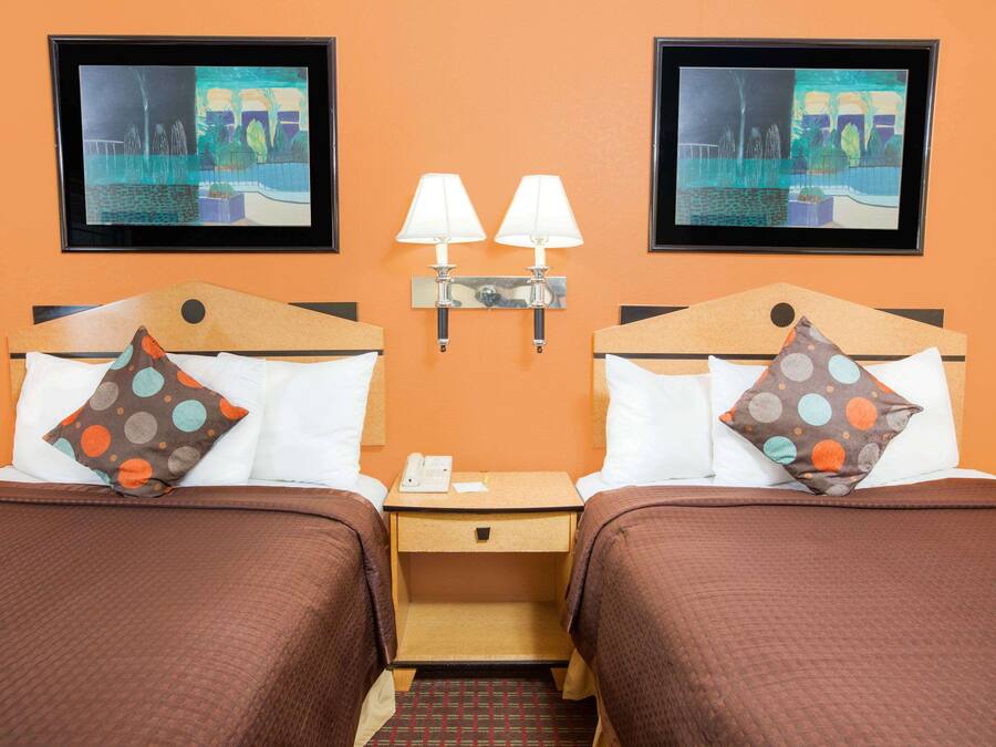 A hotel room with two beds, each with a pillow and a nightstand with a lamp.