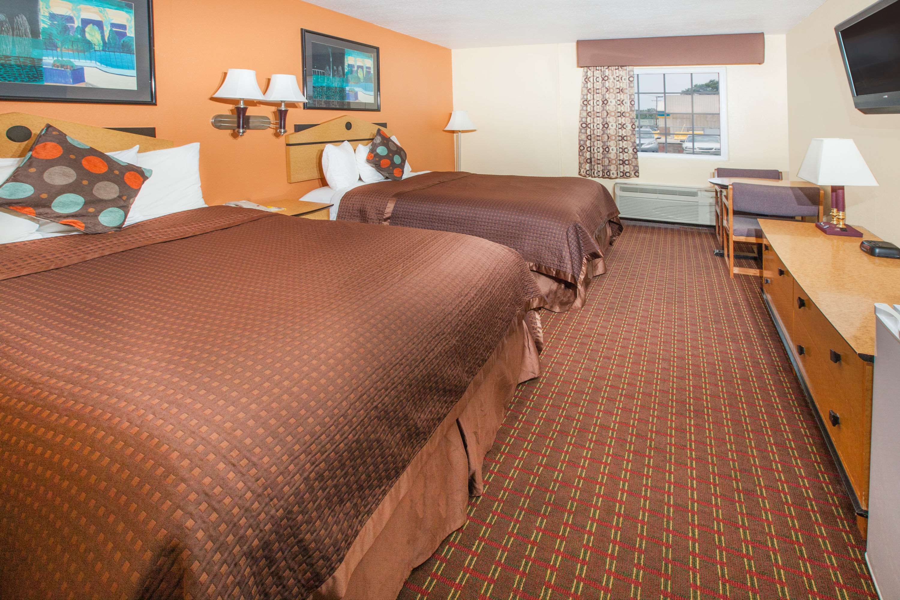 A hotel room with two beds, a desk, a chair, a TV, and a window with curtains.