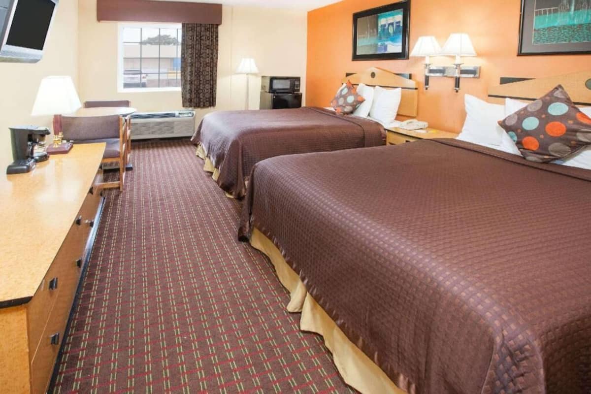 A hotel room with two beds, a desk, a television, and a window.