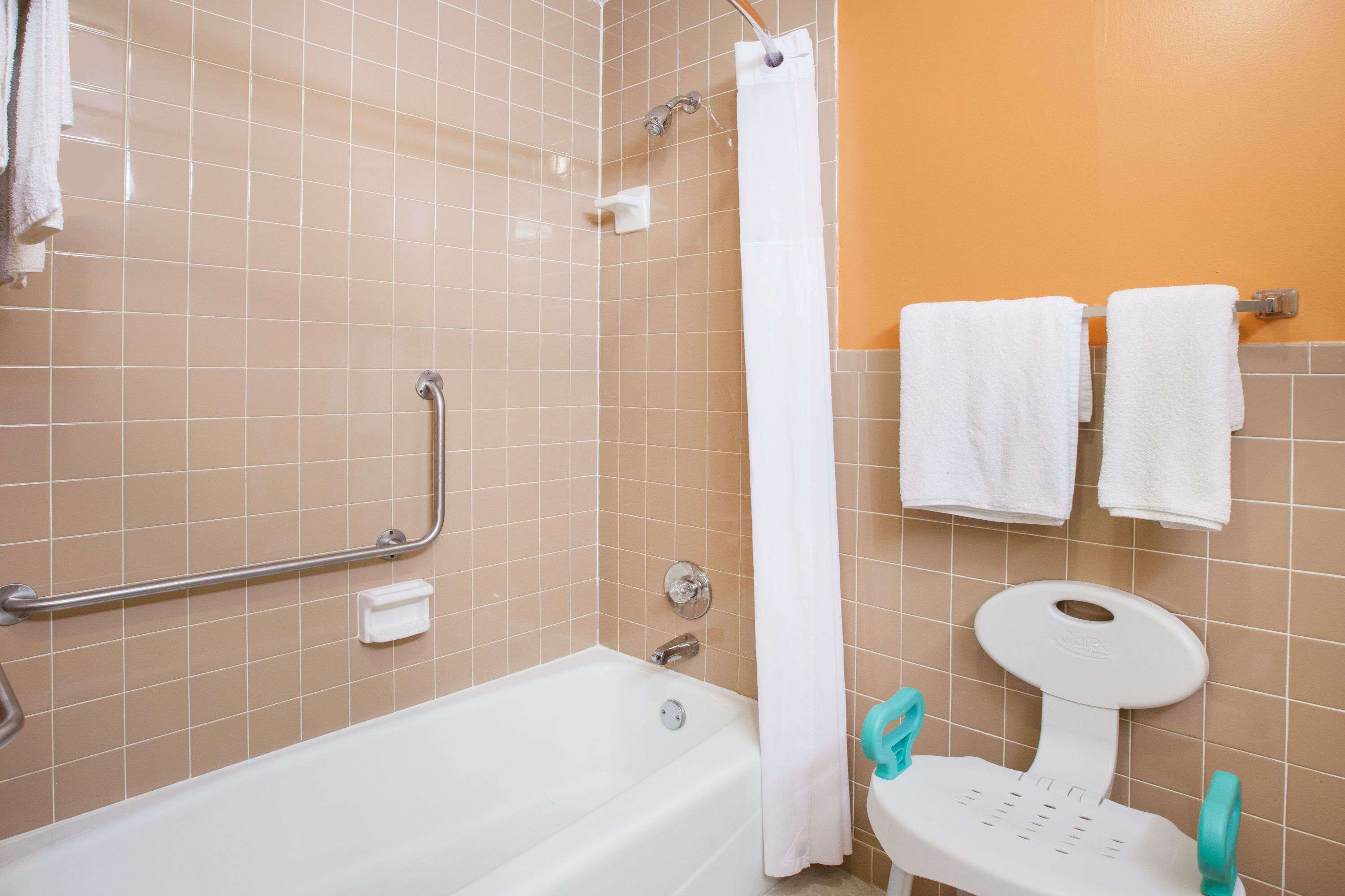 A bathroom with a bathtub, a shower with a curtain, a grab bar, and a toilet with a safety seat.