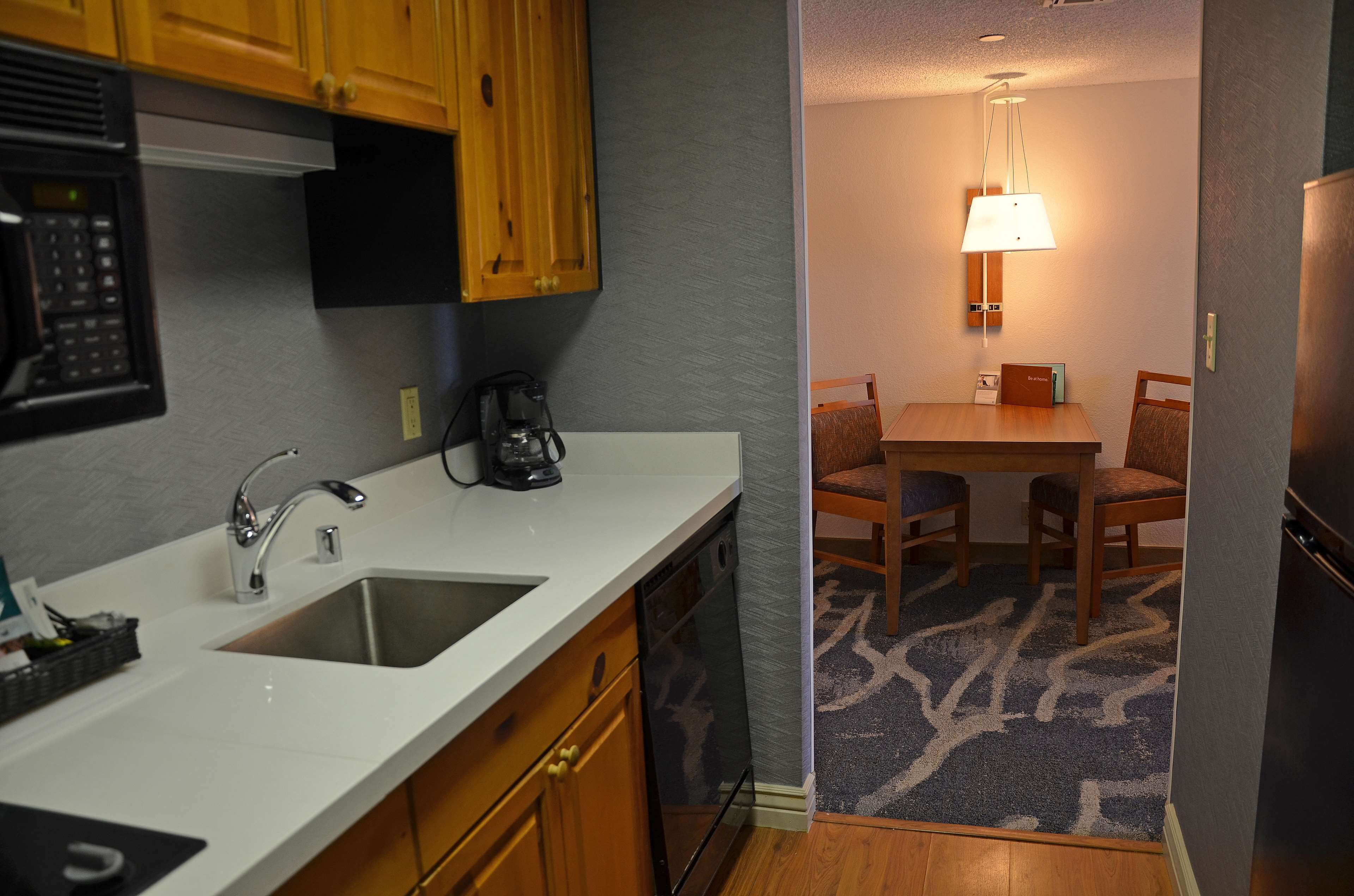 A compact kitchen with a sink, stove, and microwave. There is a dining area with a table and chairs, and a lamp above the table.