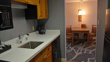 A compact kitchen with a sink, stove, and microwave. There is a dining area with a table and chairs, and a lamp above the table.
