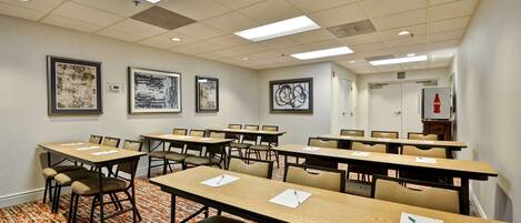 A conference room with multiple tables and chairs, framed artwork on the walls, and a patterned carpet.