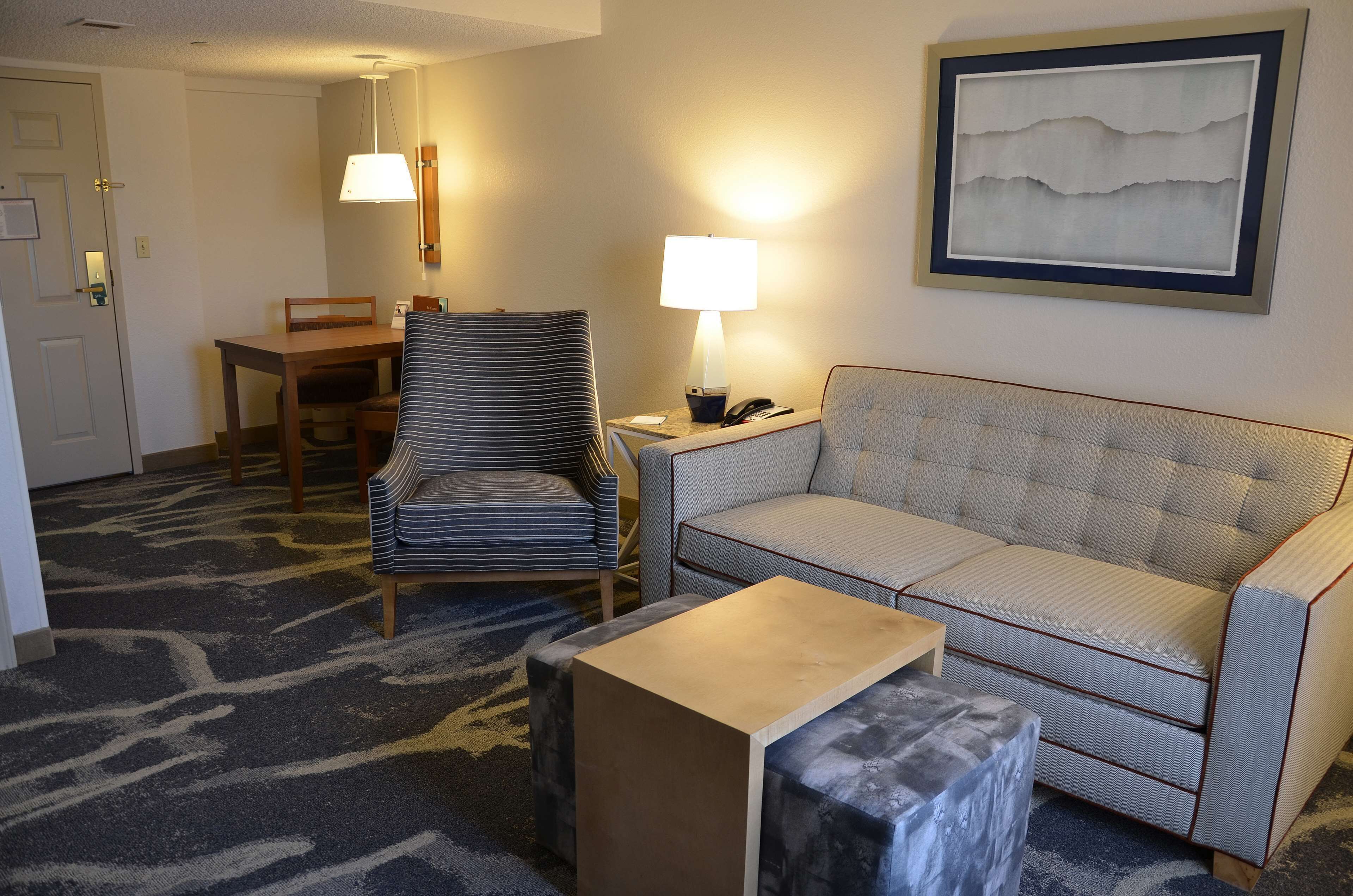 A hotel room with a striped armchair, a sofa, a small table, a lamp, and a framed artwork on the wall.