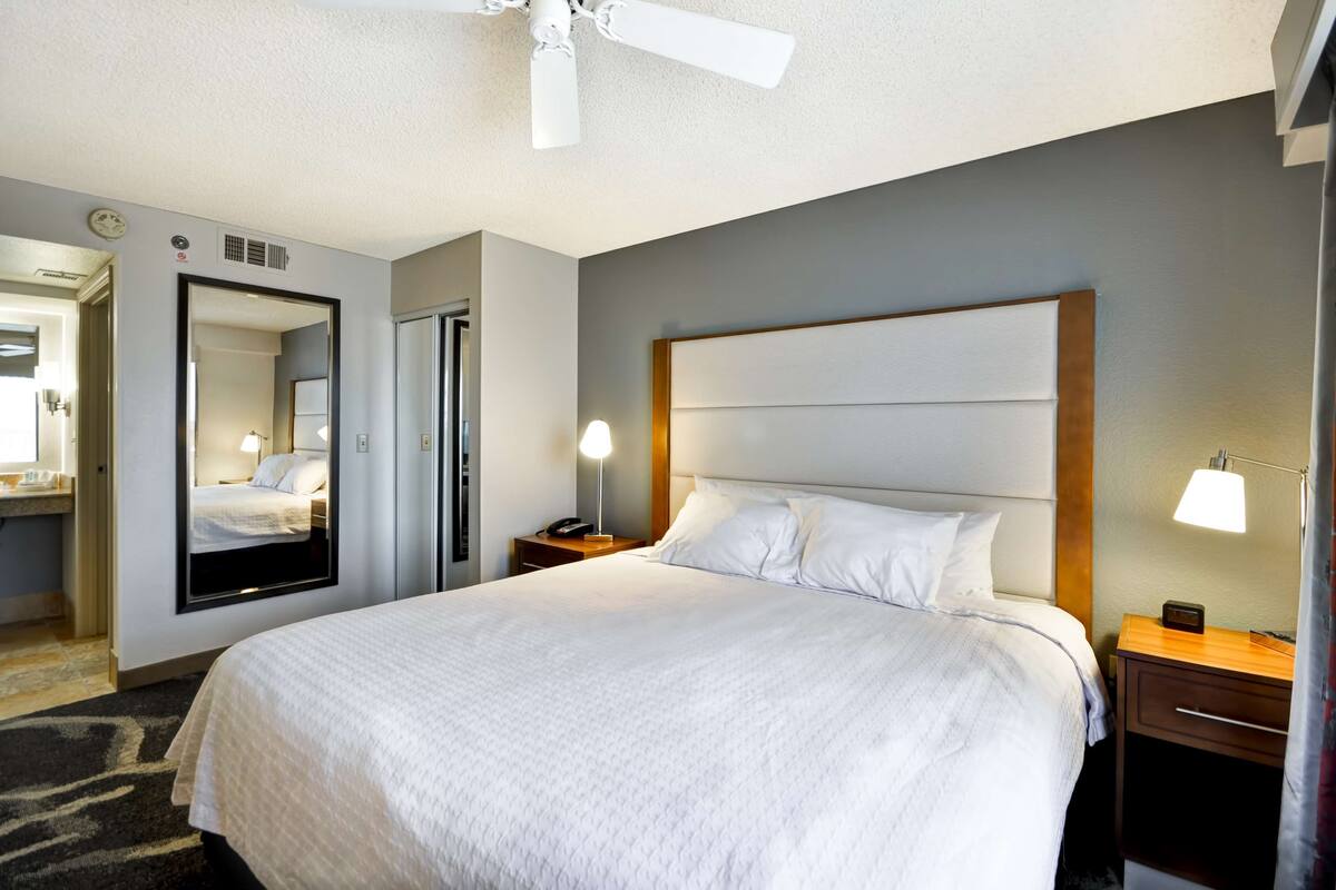 A hotel room with a large bed, two bedside tables, a ceiling fan, and a mirror on the wall.