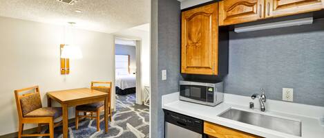 Una habitación de hotel compacta con kitchenette, un área de comedor con mesa y sillas, y una cama visible al fondo.