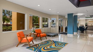 A modern lobby with orange chairs, a colorful rug, and a view of the outdoors. - Quality Inn - Near Serenoa Golf Club (Sarasota)