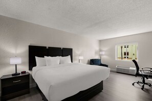 Une chambre d’hôtel avec un grand lit, des tables de chevet avec des lampes, une chaise et une fenêtre donnant sur l’extérieur.