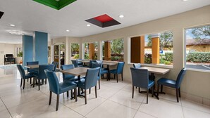 A spacious indoor area with multiple tables and chairs, large windows offering views of greenery and buildings, and a ceiling with geometric patterns. - Quality Inn - Near Serenoa Golf Club (Sarasota)