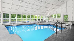 An indoor swimming pool with a clear view of the outdoors, surrounded by lounge chairs and a covered area with a grid-like ceiling. - Spark by Hilton Duluth (Duluth)