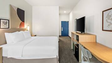 A hotel room with a bed, a desk, a television, and a door.