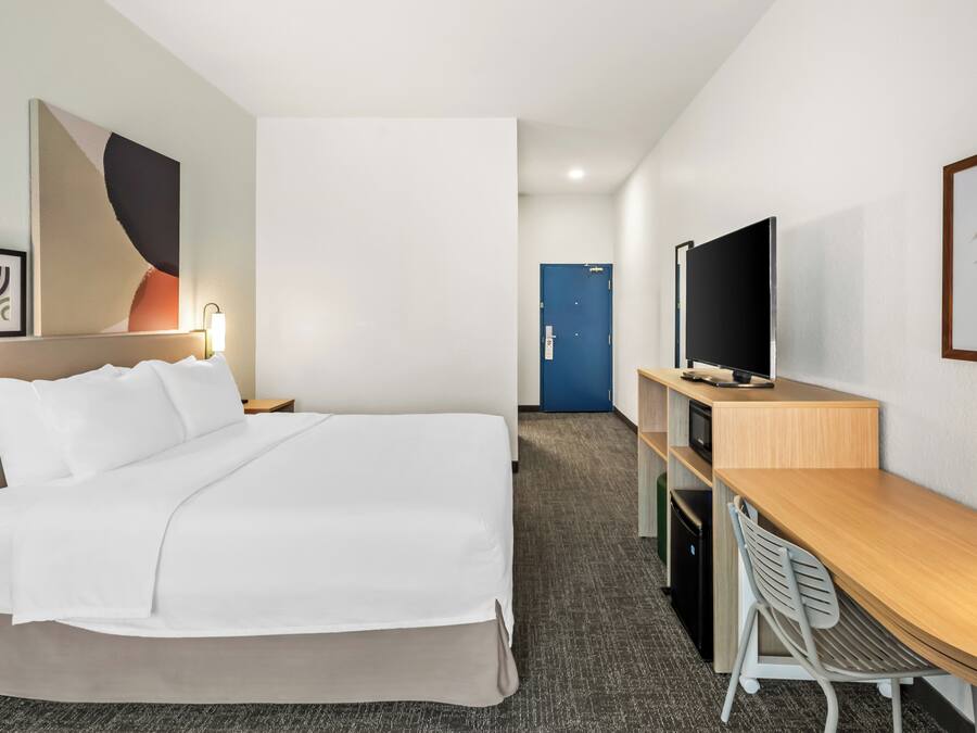 A hotel room with a bed, a desk, a television, and a door.