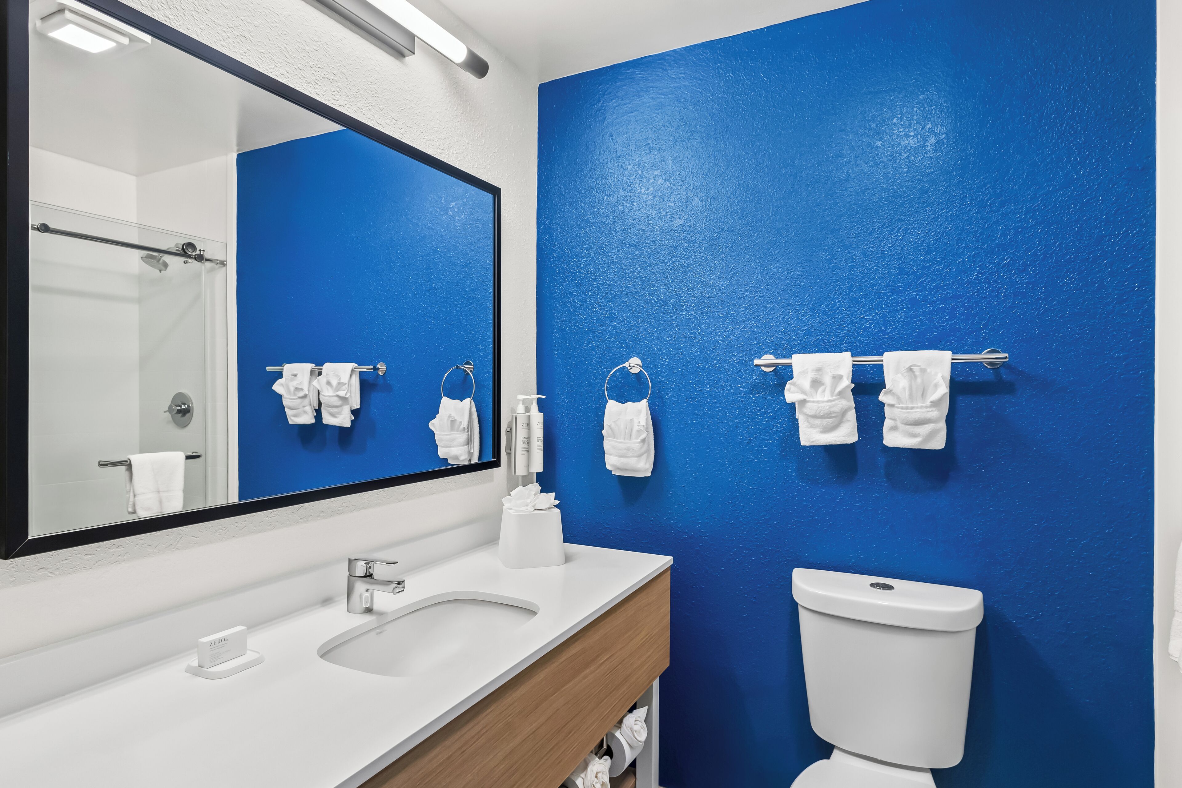 A bathroom with a white sink, a mirror, a blue wall, and a toilet.