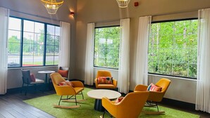 A modern lounge with large windows, yellow chairs, a round table, and two hanging lights. - Spark by Hilton Duluth (Duluth)