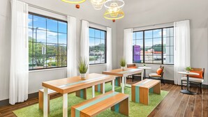 A modern room with large windows, wooden tables, benches, and a green rug. - Spark by Hilton Duluth (Duluth)