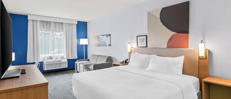 Habitación de hotel con una cama grande, un escritorio con una computadora portátil, una silla, una lámpara de escritorio y un televisor montado en la pared.