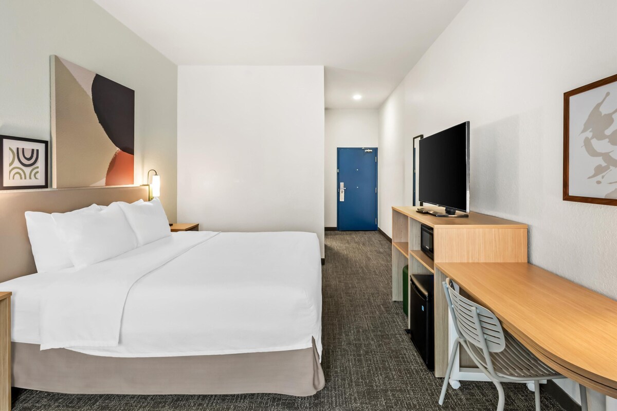 Una habitación de hotel con cama, escritorio, televisión y puerta.