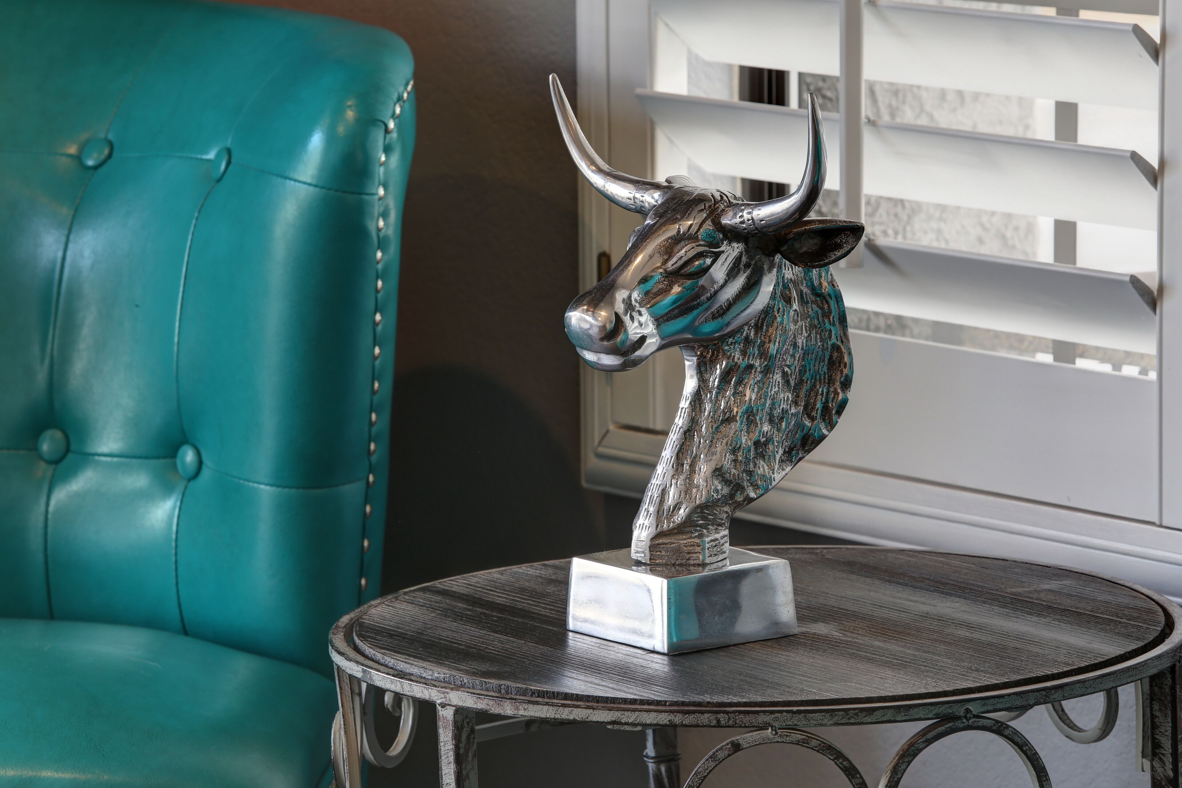 A teal leather chair and a metal table with a bull head sculpture.