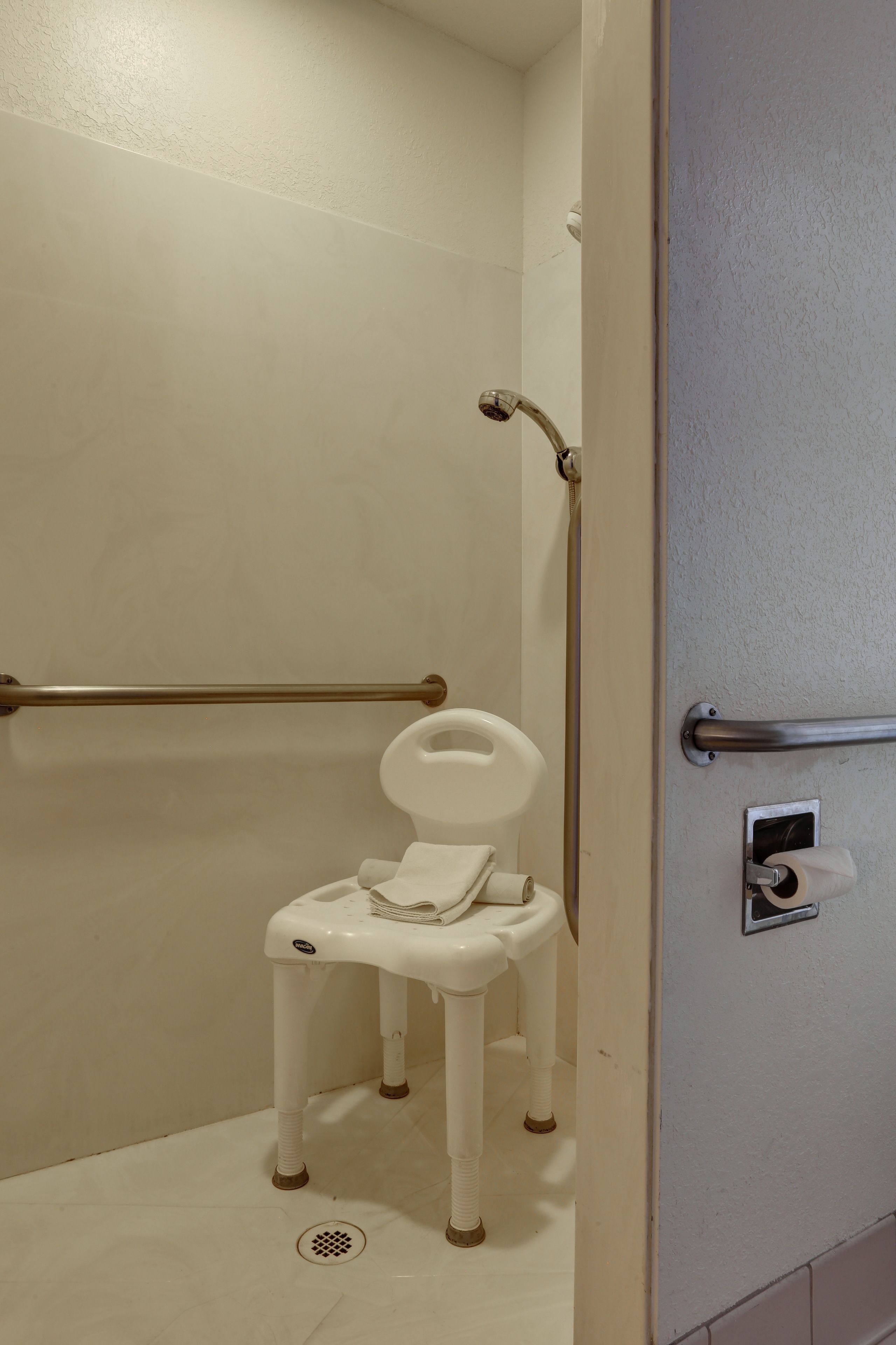 Un baño con inodoro blanco, barras de apoyo y zona de ducha.