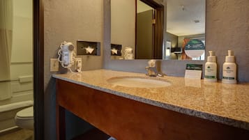 A bathroom with a granite countertop, a sink, a hairdryer, and two bottles of body lotion.