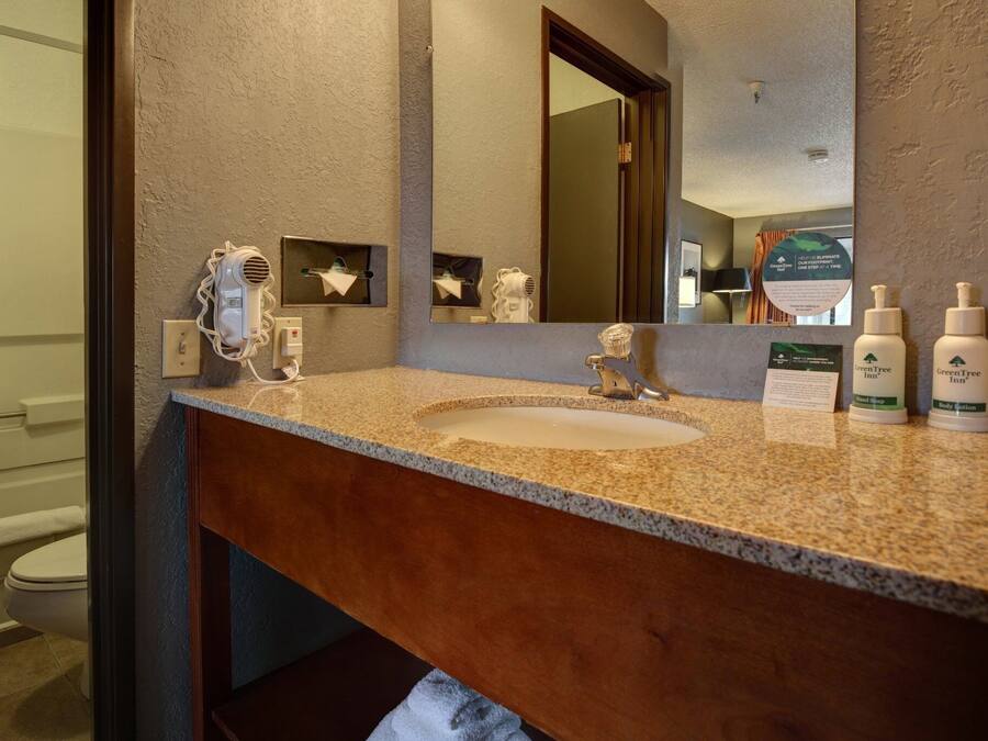 A bathroom with a granite countertop, a sink, a hairdryer, and two bottles of body lotion.