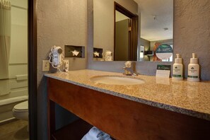 A bathroom with a granite countertop, a sink, a hairdryer, and two bottles of body lotion.