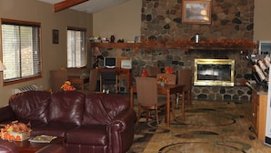 A living room with a stone fireplace, leather sofa, and a dining area with wicker chairs. - Boarders Inn & Suites by Cobblestone Hotels - Ripon (Ripon)