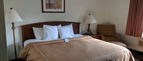 A hotel room with a large bed, two bedside lamps, a chair, a framed picture on the wall, and a window with curtains.