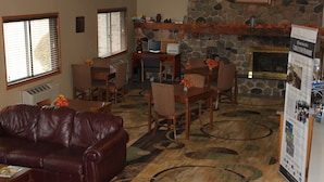 A living room with a brown leather couch, dining table with chairs, a fireplace, and a stone wall. - Boarders Inn & Suites by Cobblestone Hotels - Ripon (Ripon)