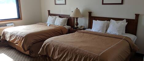 A hotel room with two beds, each with brown bedding, a nightstand with a lamp, and framed pictures on the wall.