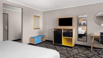 Habitació d'hotel amb llit, escriptori, televisió, nevera i mirall.