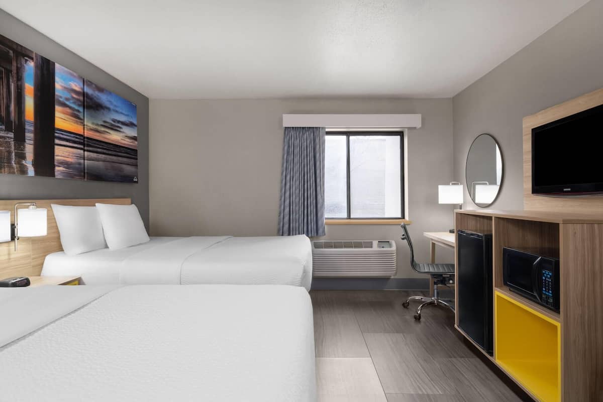 A hotel room with two beds, a TV, a desk, a chair, and a window with curtains.