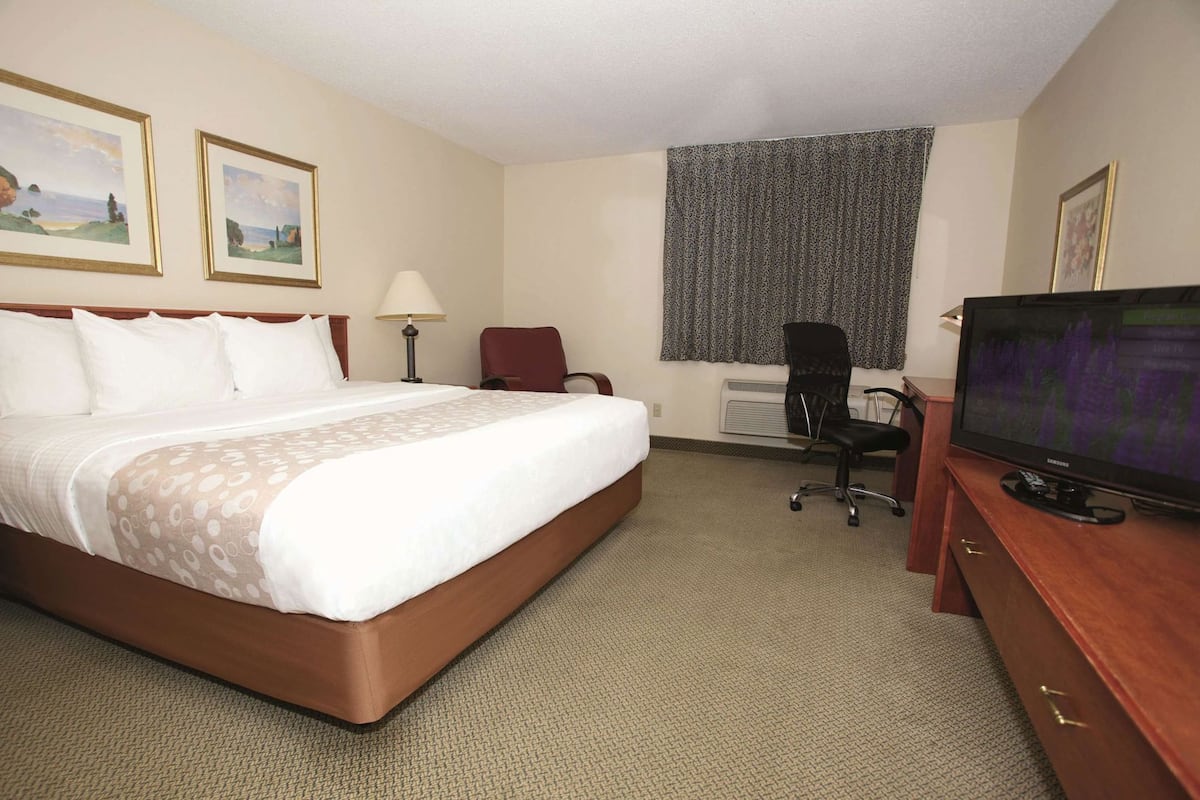 A hotel room with a large bed, a desk with a computer, a television, and two framed pictures on the wall.