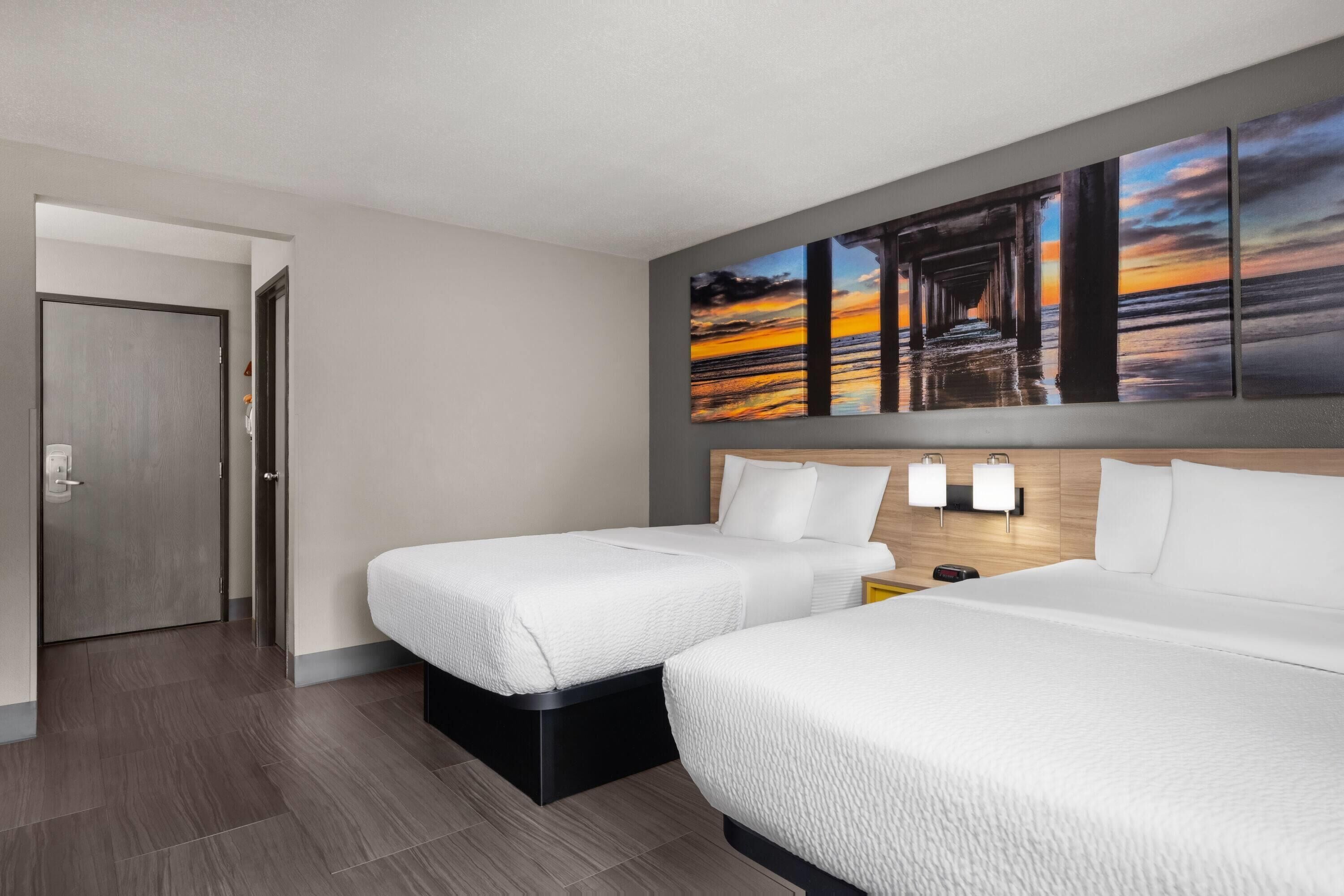 A hotel room with two beds, a wooden headboard, a wall-mounted artwork, and a door.