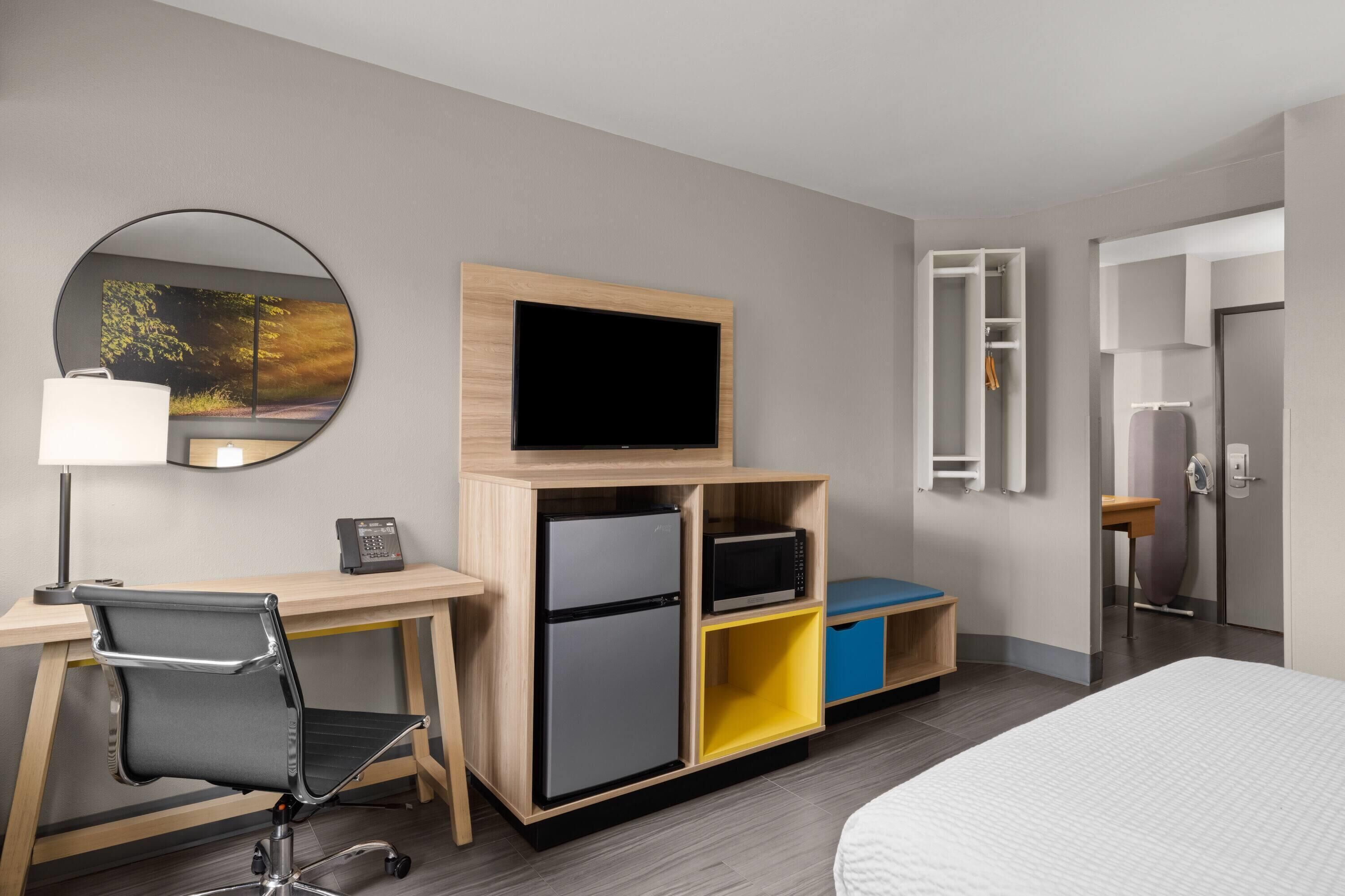 A hotel room with a bed, a desk with a chair, a television, a refrigerator, a microwave, and a wardrobe.