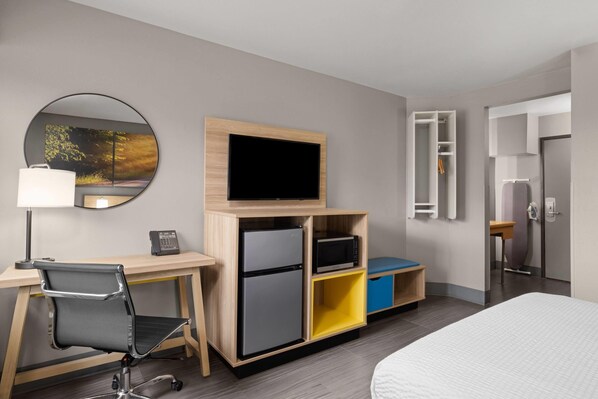 A hotel room with a bed, a desk with a chair, a television, a refrigerator, a microwave, and a wardrobe.