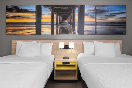 A hotel room with two beds, a nightstand with a clock, and a wall-mounted artwork of a pier at sunset.. La Quinta Inn by Wyndham Milwaukee Airport / Oak Creek