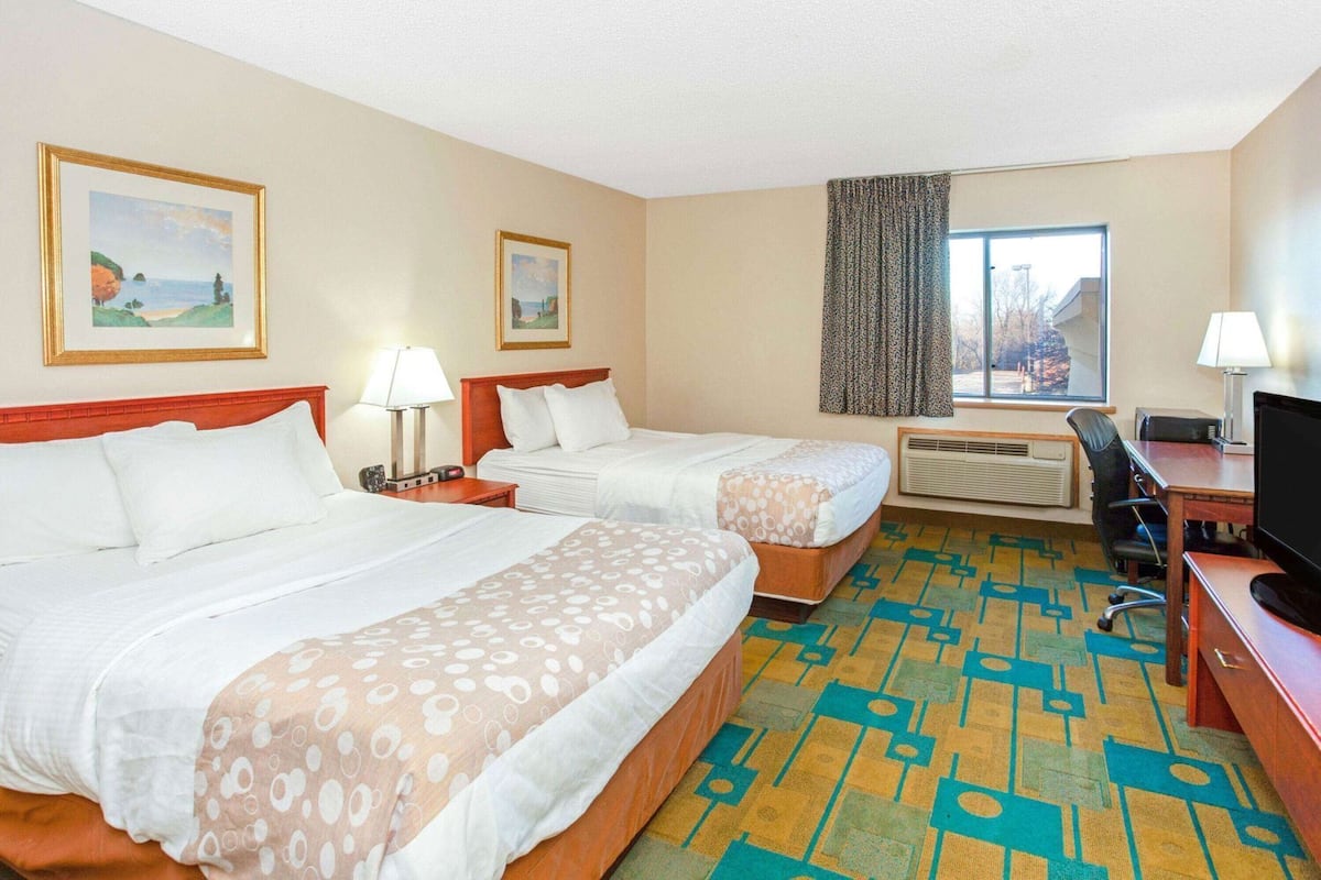 A hotel room with two beds, a desk, a television, and a window with a view.
