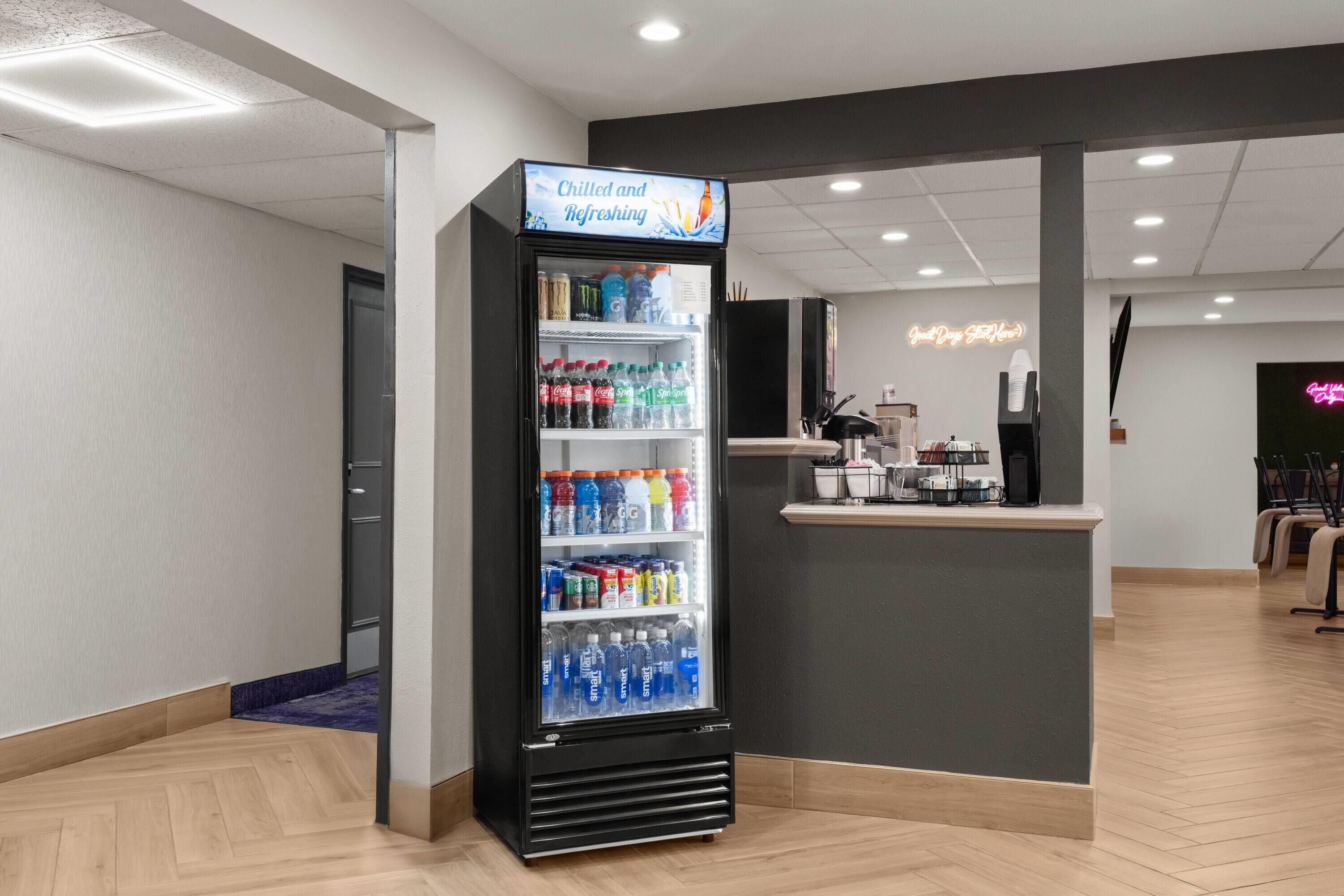 Un vestíbulo de hotel con dispensador de bebidas de autoservicio, un mostrador de recepción y un letrero de neón.