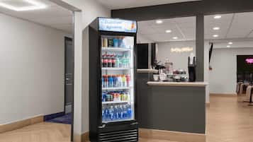 Un vestíbulo de hotel con dispensador de bebidas de autoservicio, un mostrador de recepción y un letrero de neón.