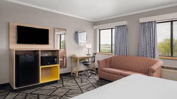A hotel room with a bed, a TV, a desk, a chair, a sofa, a mirror, and a window with curtains.