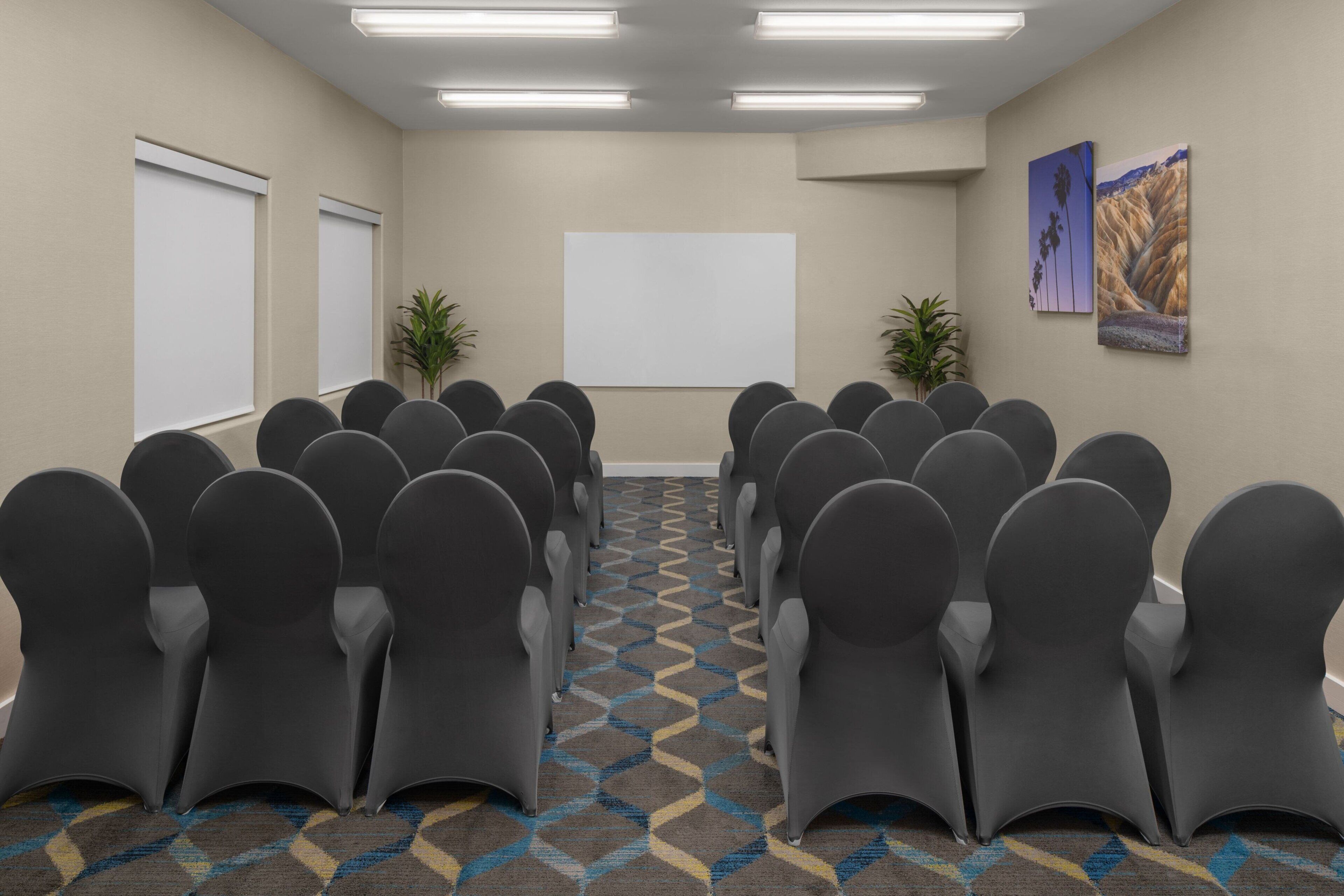 A conference room with rows of chairs, a projector screen, and two wall-mounted paintings.