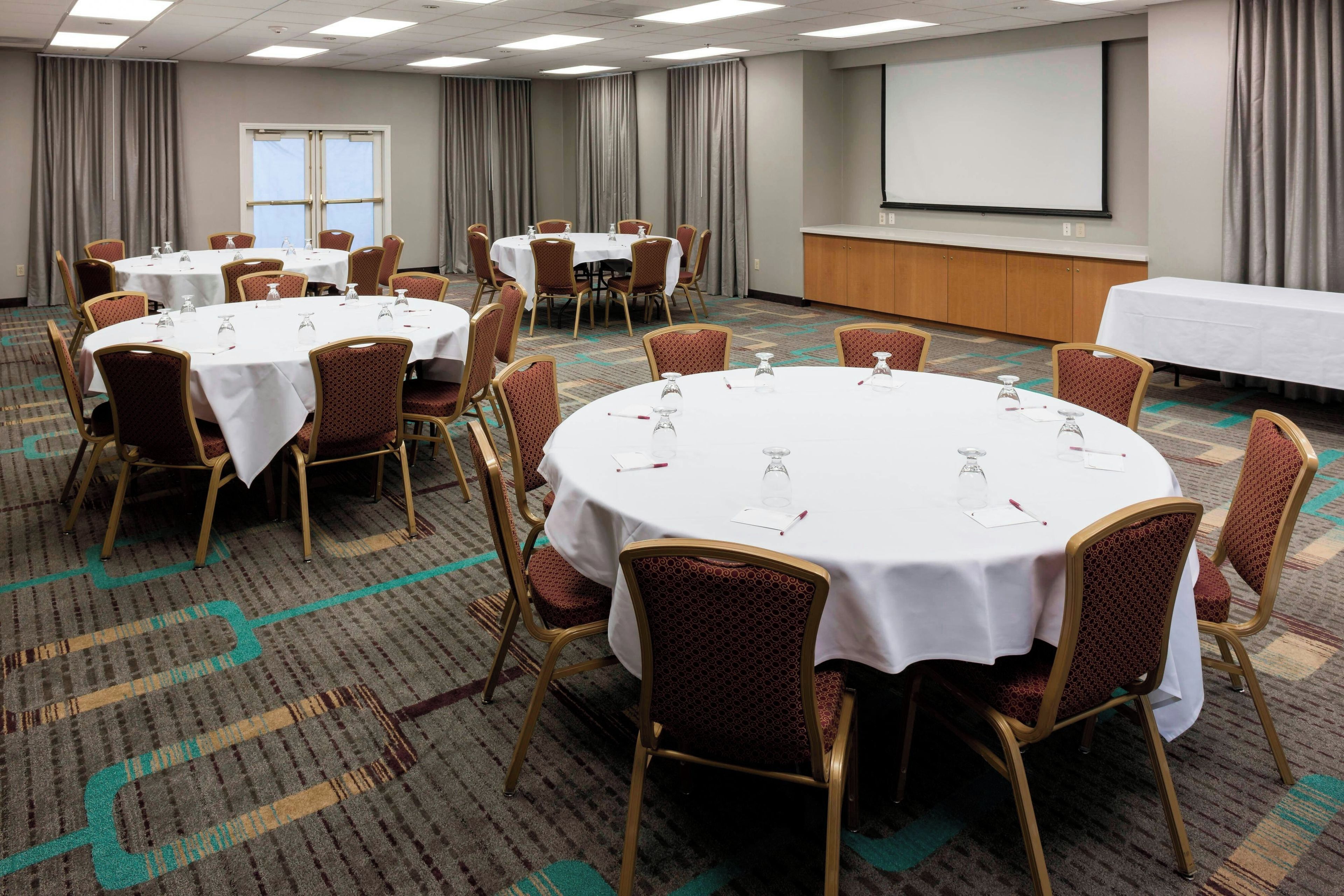 A conference room with round tables, chairs, a projector screen, and a whiteboard.
