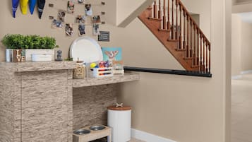 A pet-friendly area with a wooden staircase, a wall-mounted photo collage, a pet feeding station, and a small plant.