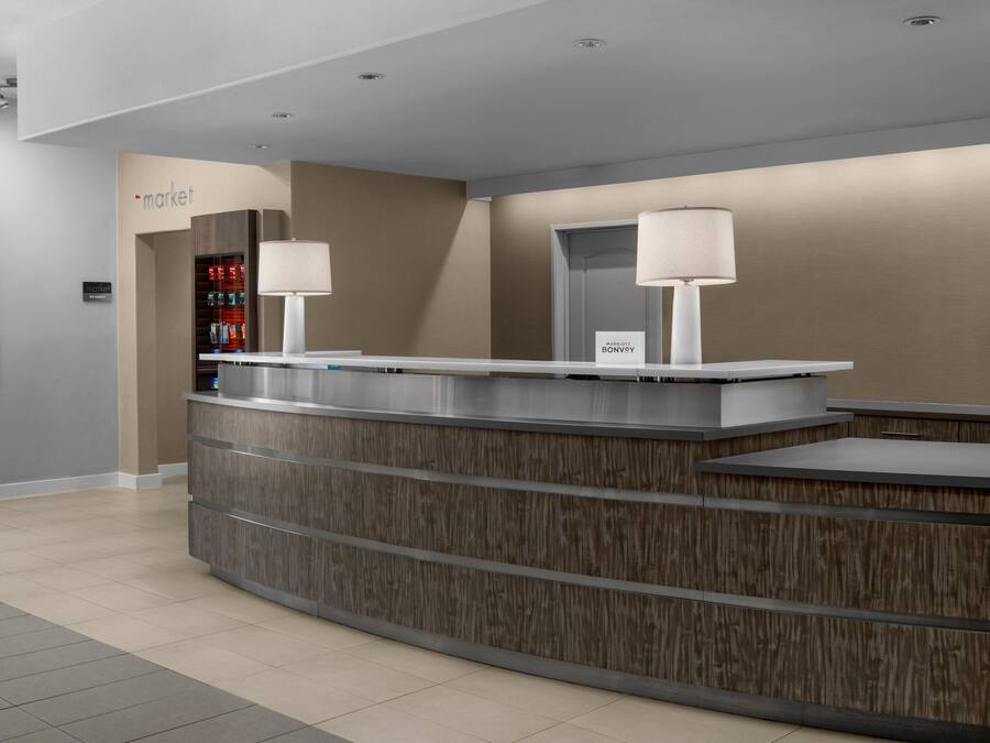 Una moderna reception con finitura in legno e due lampade. Un cartello indica che si tratta di una struttura Marriott Bonvoy.