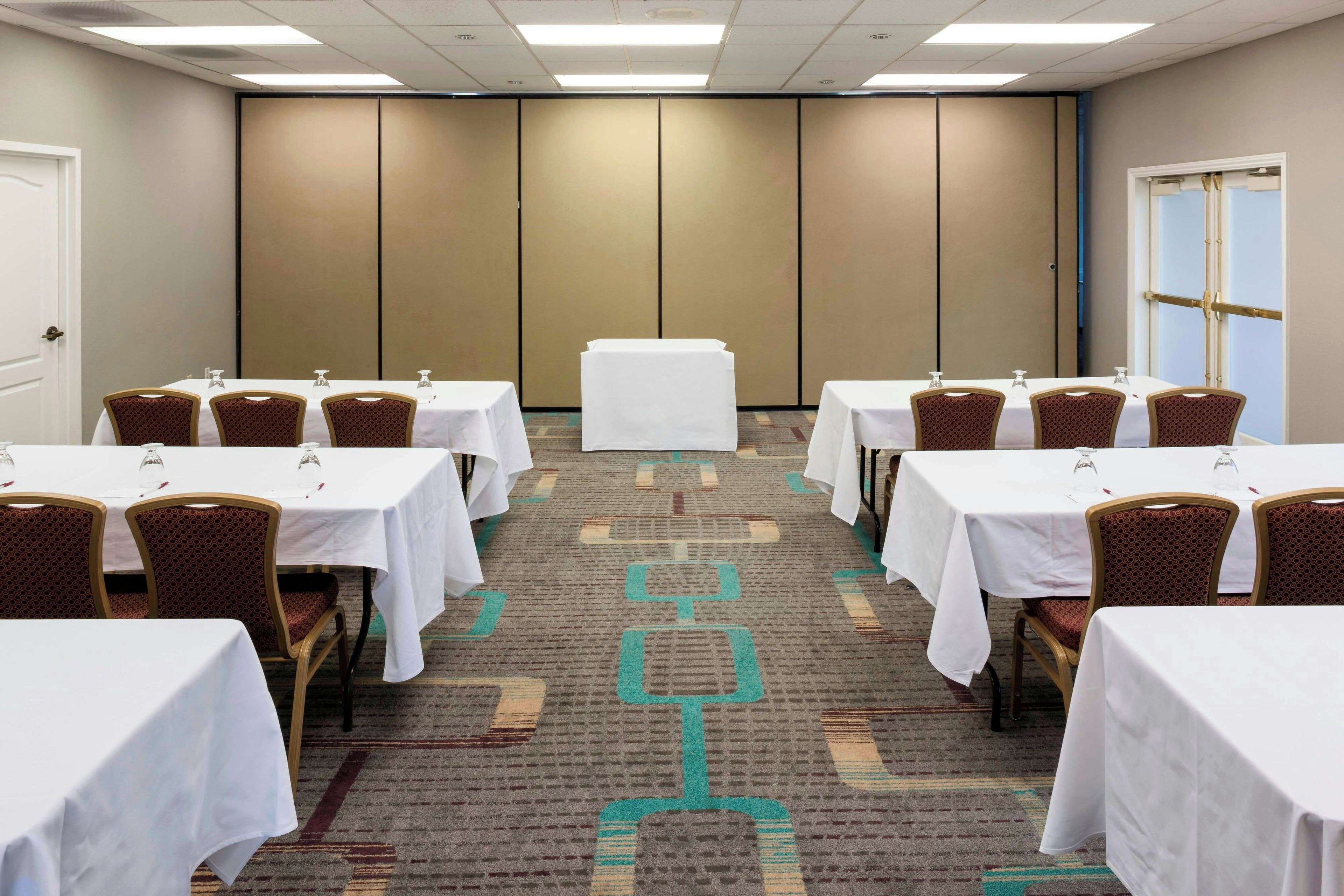 Une salle de conférence dotée de plusieurs tables et chaises, d’un sol recouvert de moquette et d’une porte située sur le côté droit.